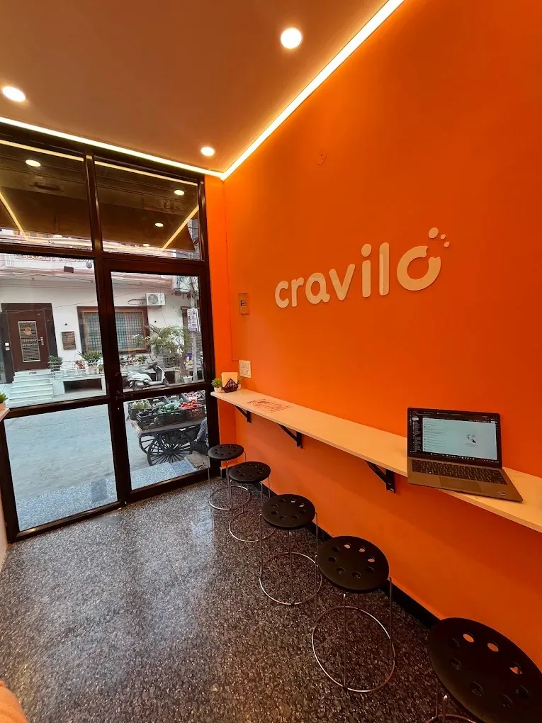 Inside Cravilo: the orange wall, a long counter by the window and a row of stools